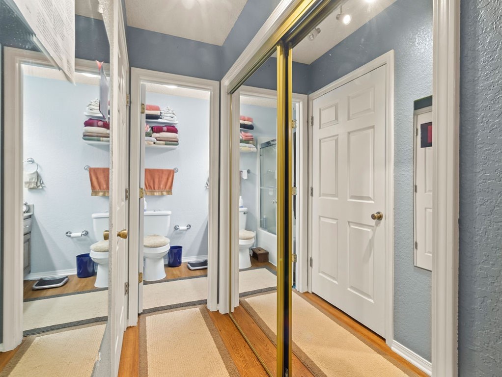 Bathroom reflected in mirrored closet doors, with a glass shower and shelves of folded towels.
