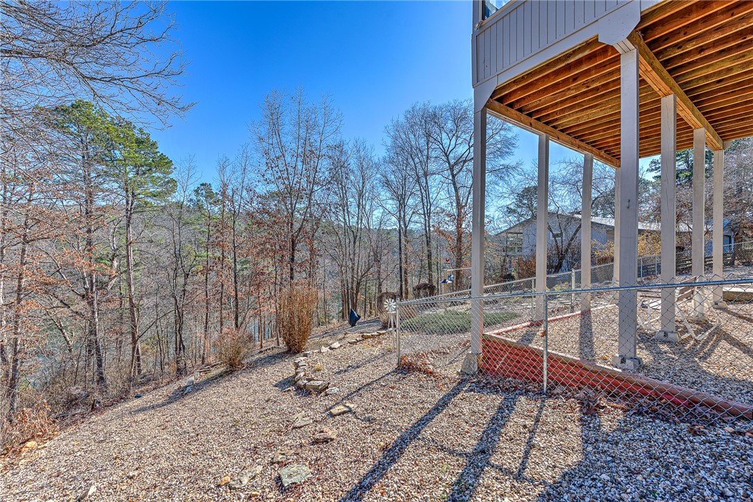 Elevated home beside a wooded slope, with a raised deck and gravel ground below.