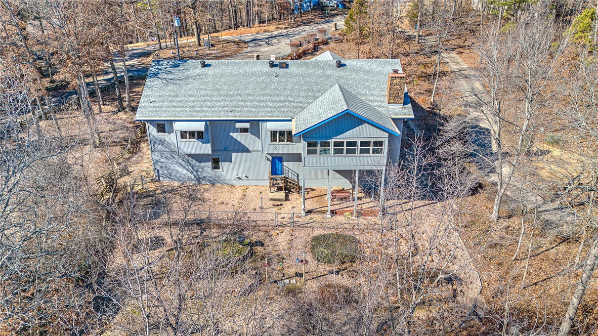 Aerial view of a blue-gray house with bright blue trim amid leafless trees.