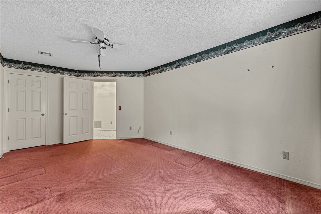 Empty bedroom with pink carpet, a ceiling fan, and paneled doors.