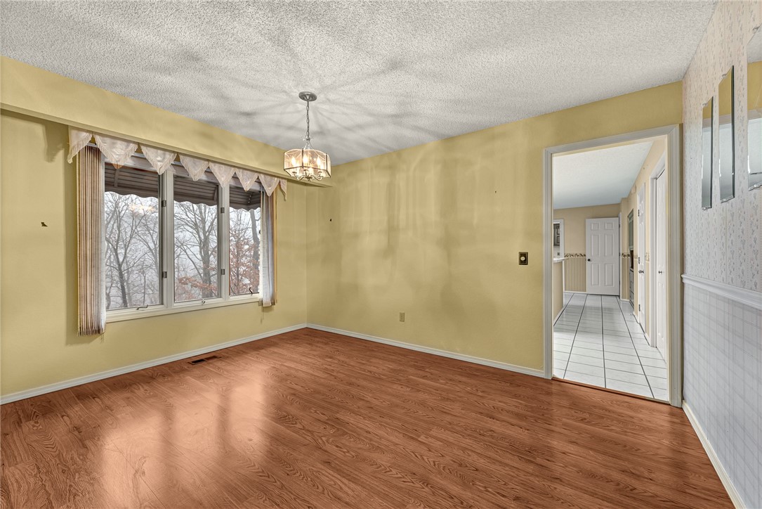 Empty dining room with yellow walls, wood flooring, a large window, and a chandelier.