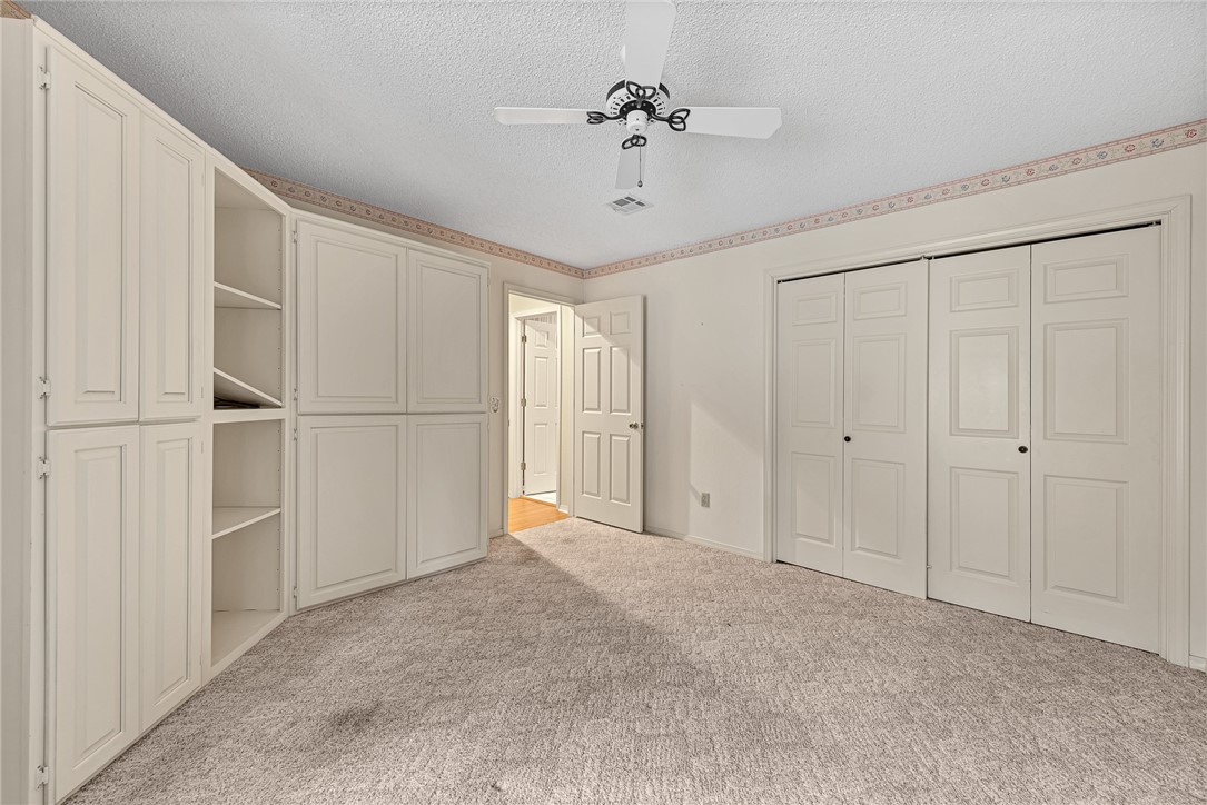 Empty bedroom with white built-in cabinets, beige carpet, and double closet doors.