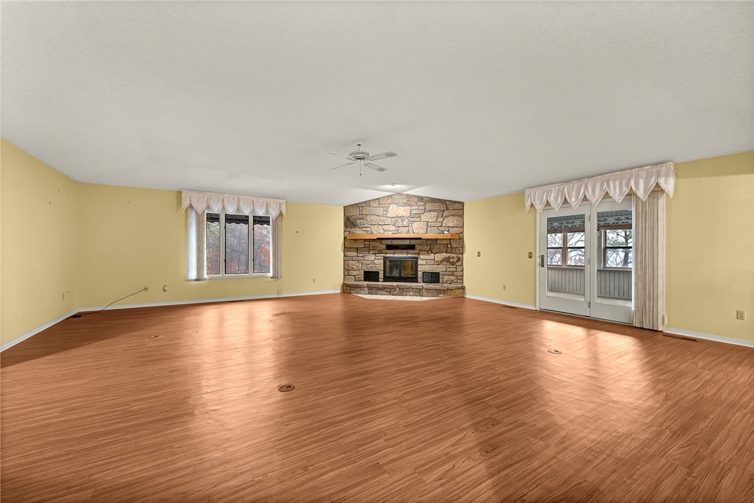 Empty living room with hardwood floors, a large stone fireplace, and glass patio doors.