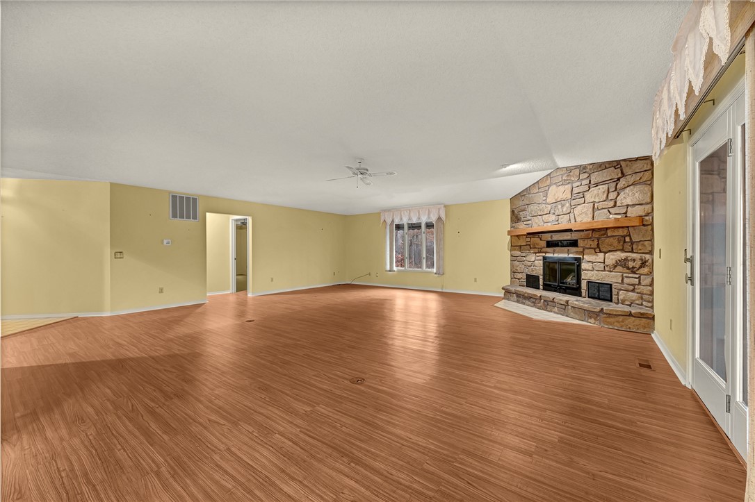 Empty living room with a large stone fireplace, wood-look flooring, and glass doors.