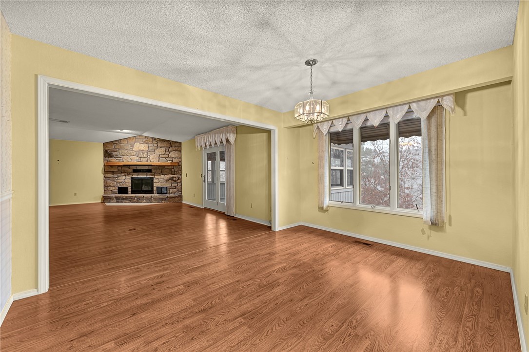 Open, vacant living and dining area with hardwood floors, a stone fireplace, and large curtained windows.