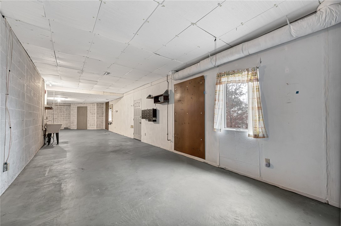 Empty garage with a concrete floor, utility sink, and pegboard beside a curtained window.