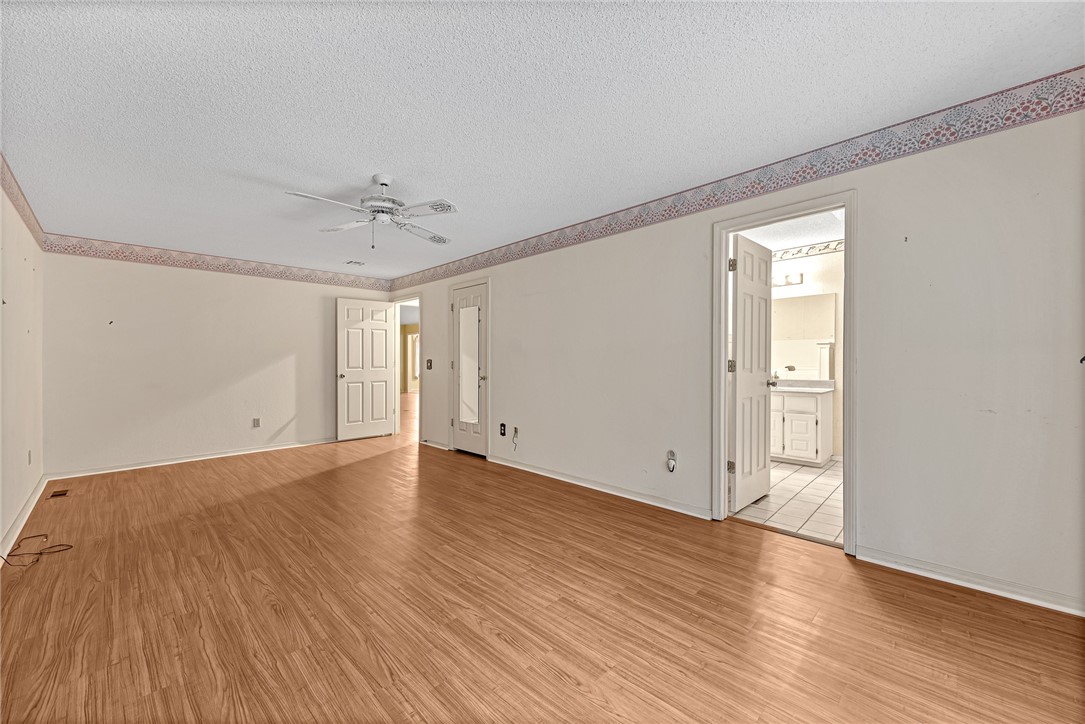 Empty room with wood-look flooring and ceiling fan, opening to a tiled bathroom.
