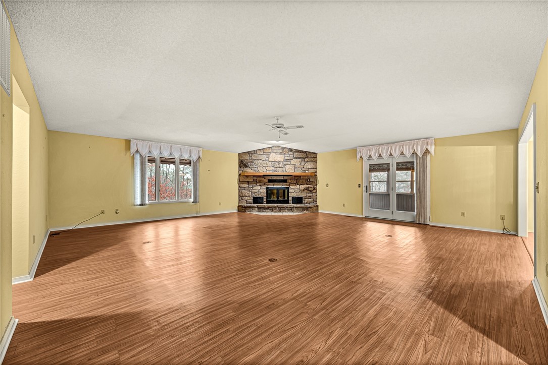Unfurnished living room with a stone fireplace, wide wood-look flooring, and windows beside glass doors.