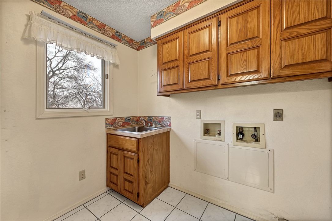 Laundry room with wooden cabinets, a utility sink, washer and dryer hookups, and a window.