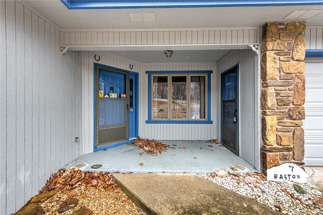 Covered home entry with blue-trimmed doors, a stone pillar, and fallen leaves.