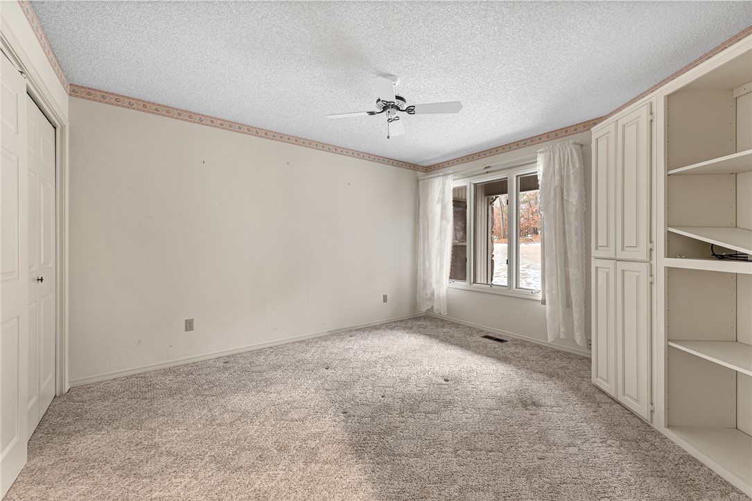 Empty bedroom with built-in white wardrobes, beige carpet, and a curtained window.
