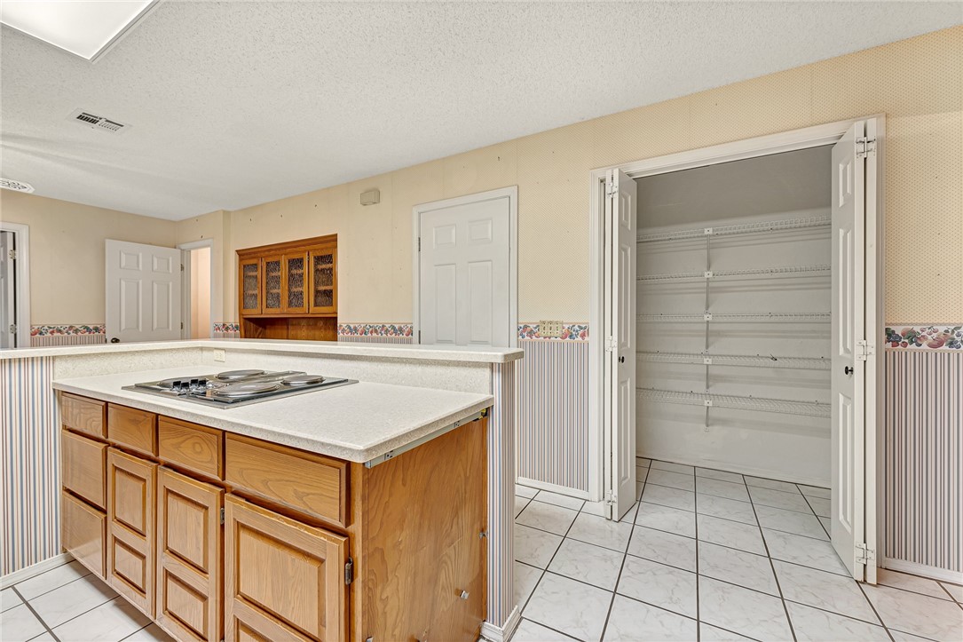 Kitchen with a wood-paneled island and cooktop beside an open pantry with wire shelves.