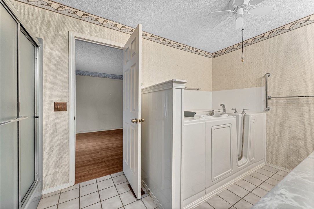 Bathroom with a white walk-in tub, glass shower, and tiled floor.