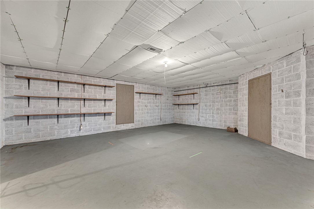 Empty block-walled storage room with concrete floor, wall shelves, and a low insulated ceiling.