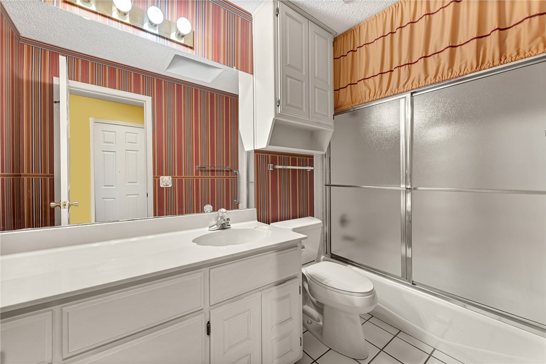 Bathroom with white vanity, toilet, and frosted-glass tub-shower beneath an orange valance.