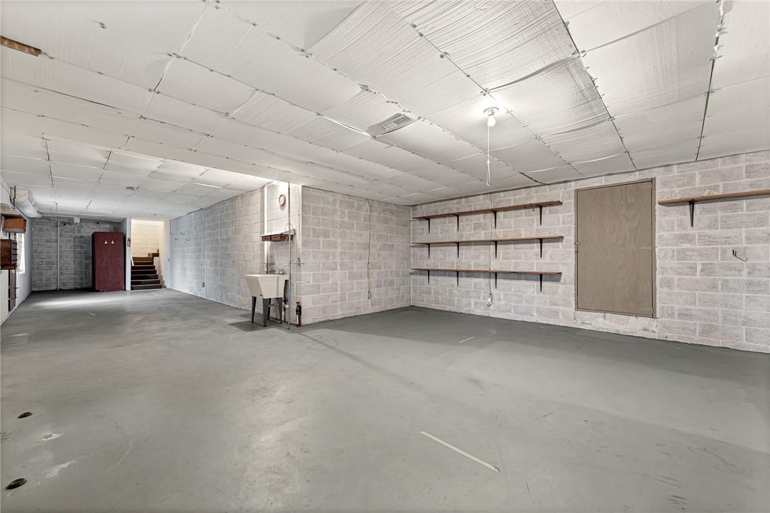 Unfinished basement with concrete floors, block walls, wall shelves, a utility sink, and stairs.