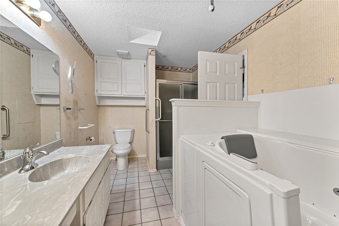 Bathroom with a large jetted tub, marble-look vanity, toilet, and glass shower.