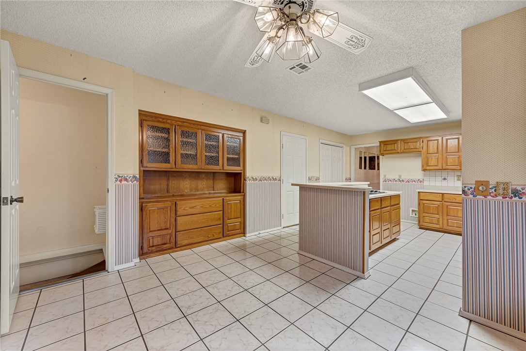 Kitchen with honey-colored wood cabinetry, a built-in hutch, central island, and large tiled floor.