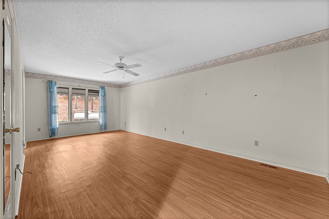 Vacant room with wood-look floors, a ceiling fan, and a wide window framed by blue curtains.