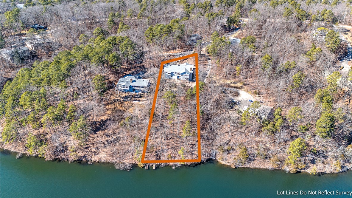 Aerial view of a wooded waterfront lot outlined in orange, with a house near the shore.