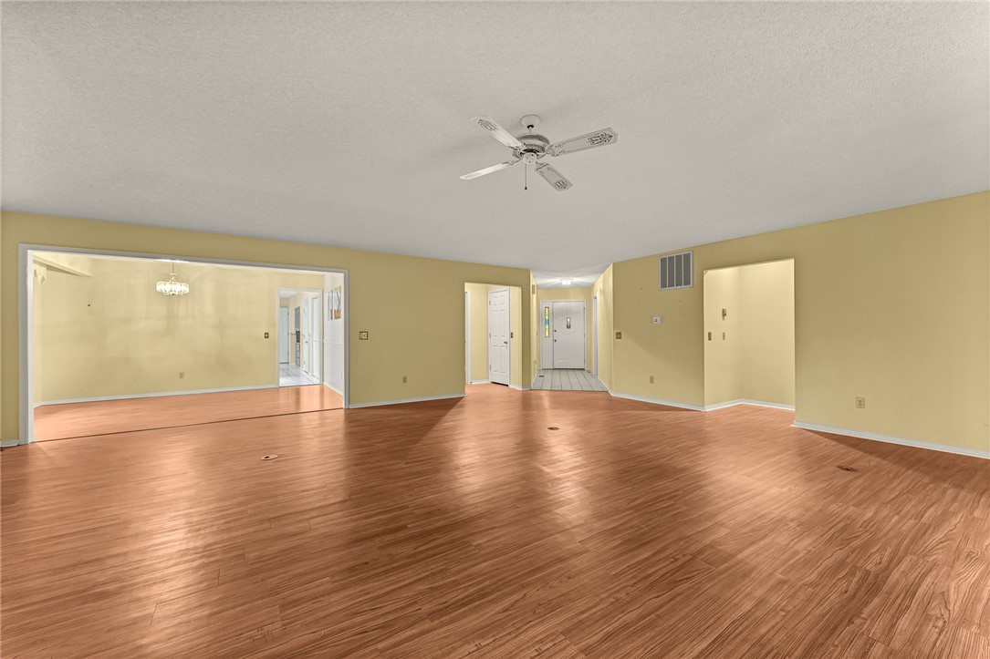 Vacant living room with wood-look flooring, pale yellow walls, and a ceiling fan.
