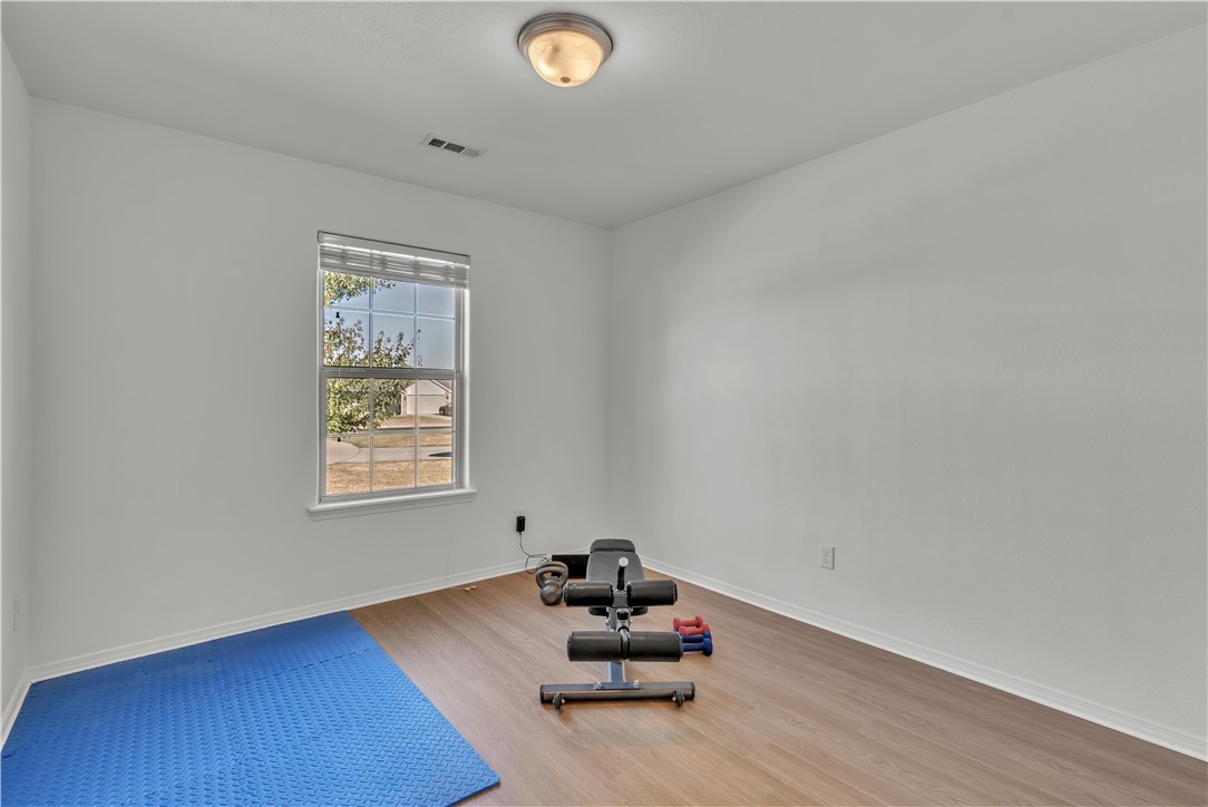 Exercise room with a blue floor mat, weight bench, and dumbbells beside a window.