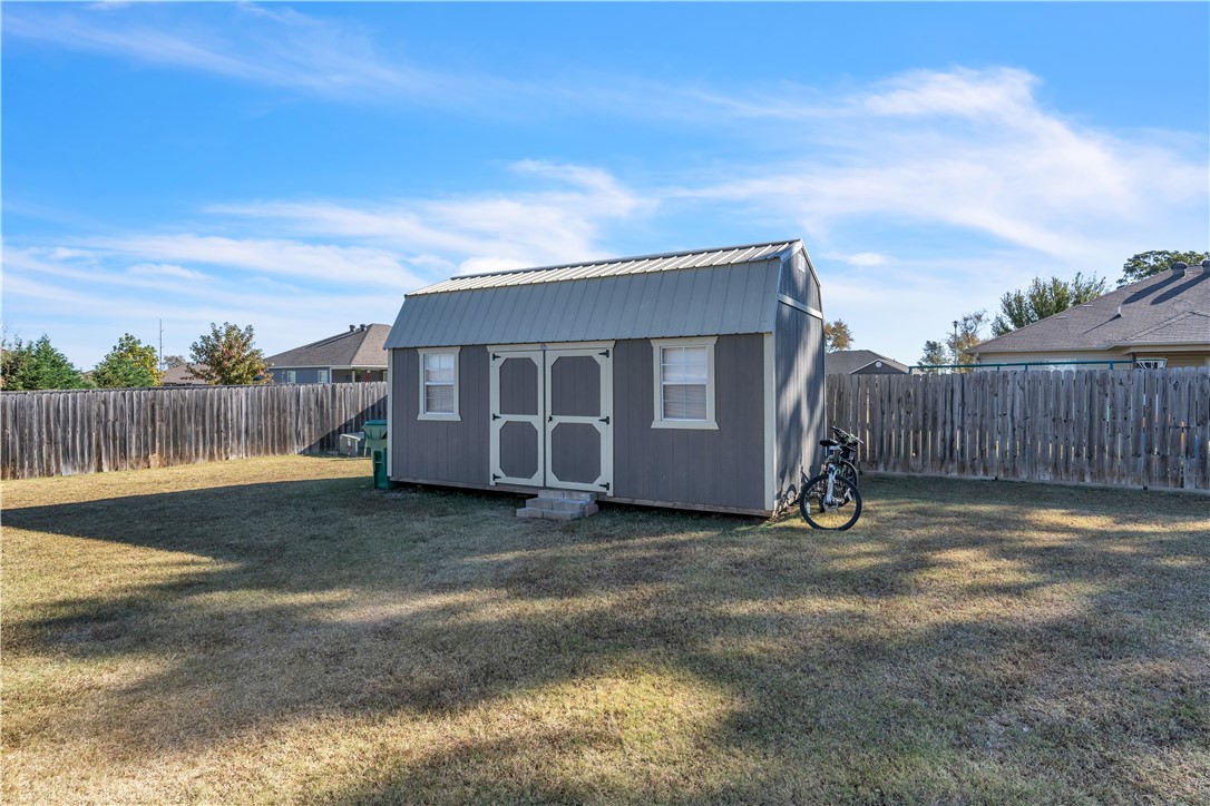 Gray backyard shed with double doors and windows in a fenced lawn; a bicycle leans beside it.