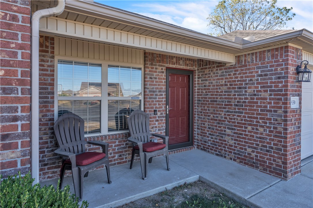 Brick home entrance with a red door, covered porch, and two chairs.