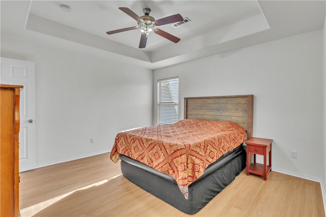 Bedroom with a red-and-gold patterned bedspread, wood headboard, and tray ceiling with ceiling fan.