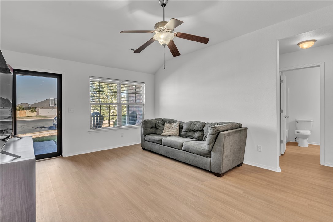 Living room with a gray sofa, ceiling fan, wood-look flooring, and an adjoining bathroom.