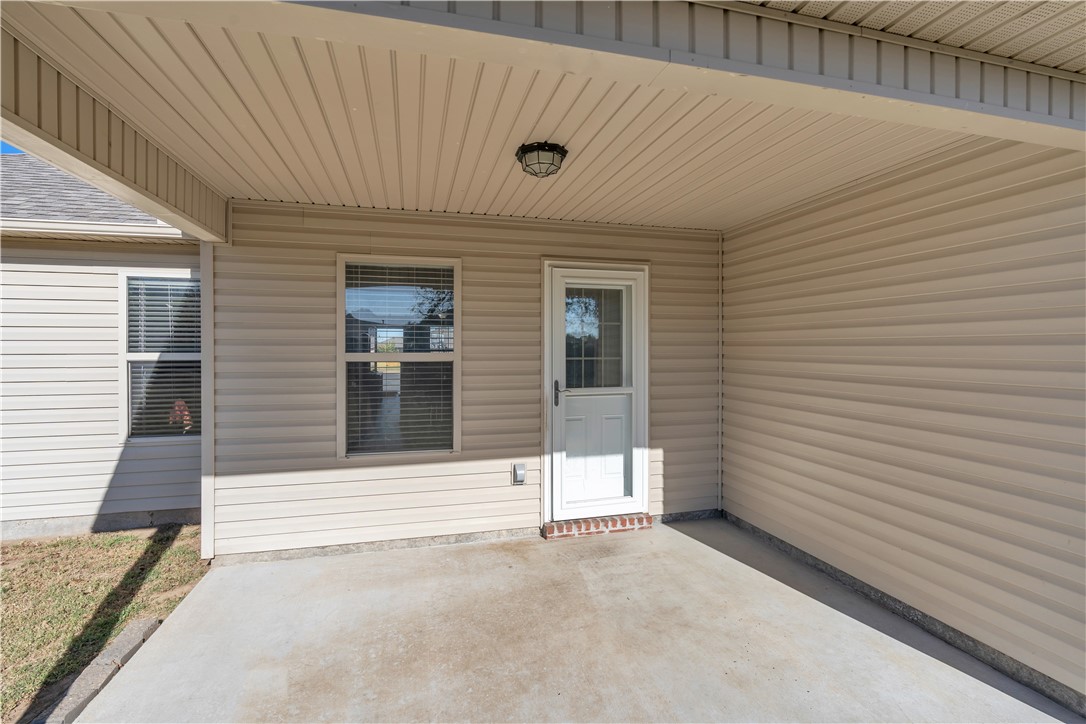 Covered concrete patio with beige siding, a white door, and a paneled ceiling.