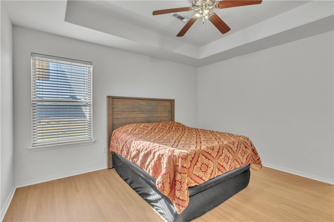 Bedroom with a red and gold quilt, rustic wood headboard, and tray ceiling.