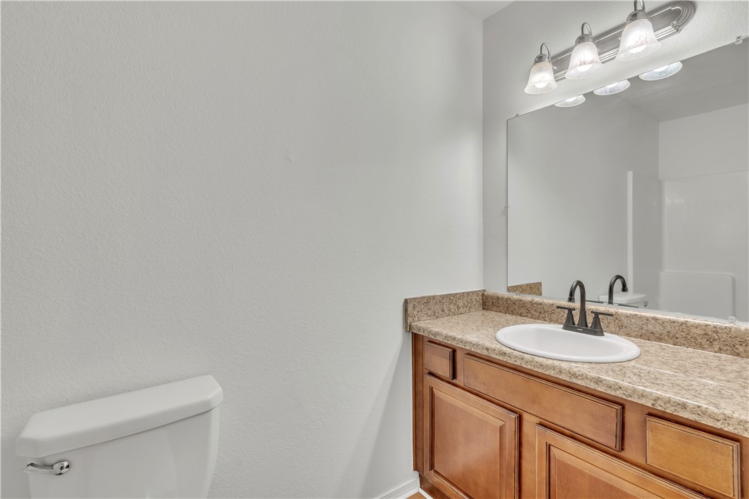 Bathroom vanity with tan countertop, oval sink, dark faucet, and toilet.