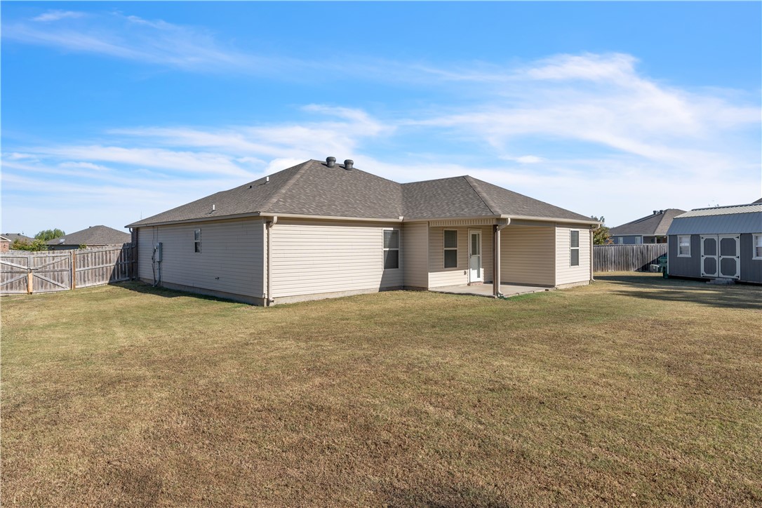 Rear of a beige single-story house with a covered patio, fenced lawn, and detached shed.