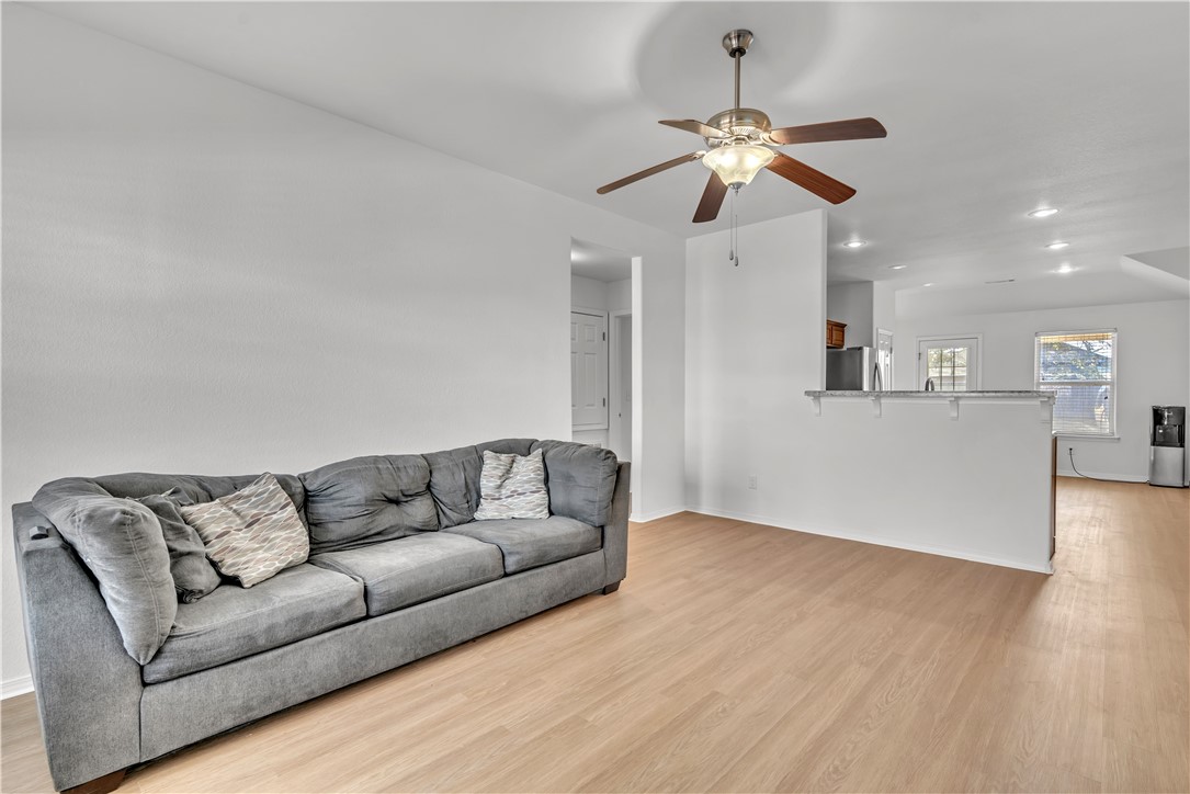 Living room with gray sofa and ceiling fan, opening to a kitchen with a breakfast bar.
