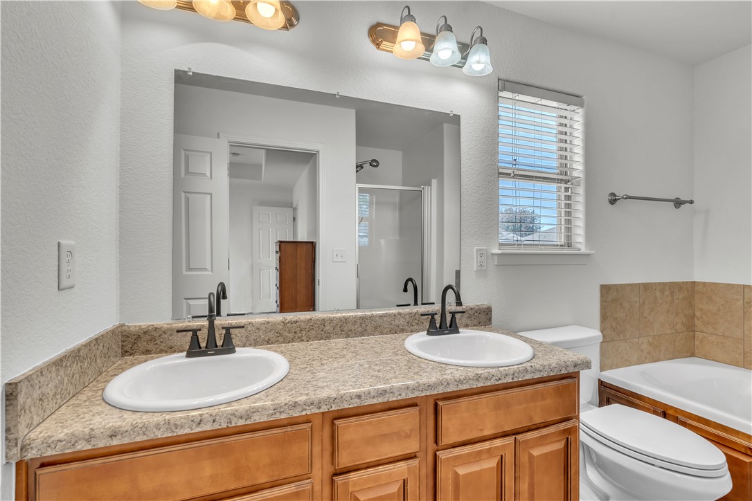 Bathroom with a double-sink wood vanity, large mirror, and bathtub beside a window.