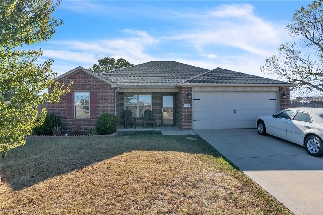 Single-story brick home with a white garage door, two chairs by the entry, and a car in the driveway.