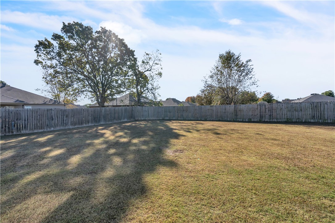 Fenced backyard with a broad lawn, mature trees, and neighboring rooftops beyond the fence.