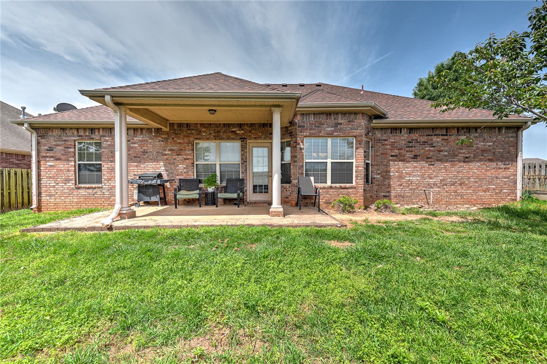Brick home’s rear exterior with a covered patio, outdoor seating, and a grill.