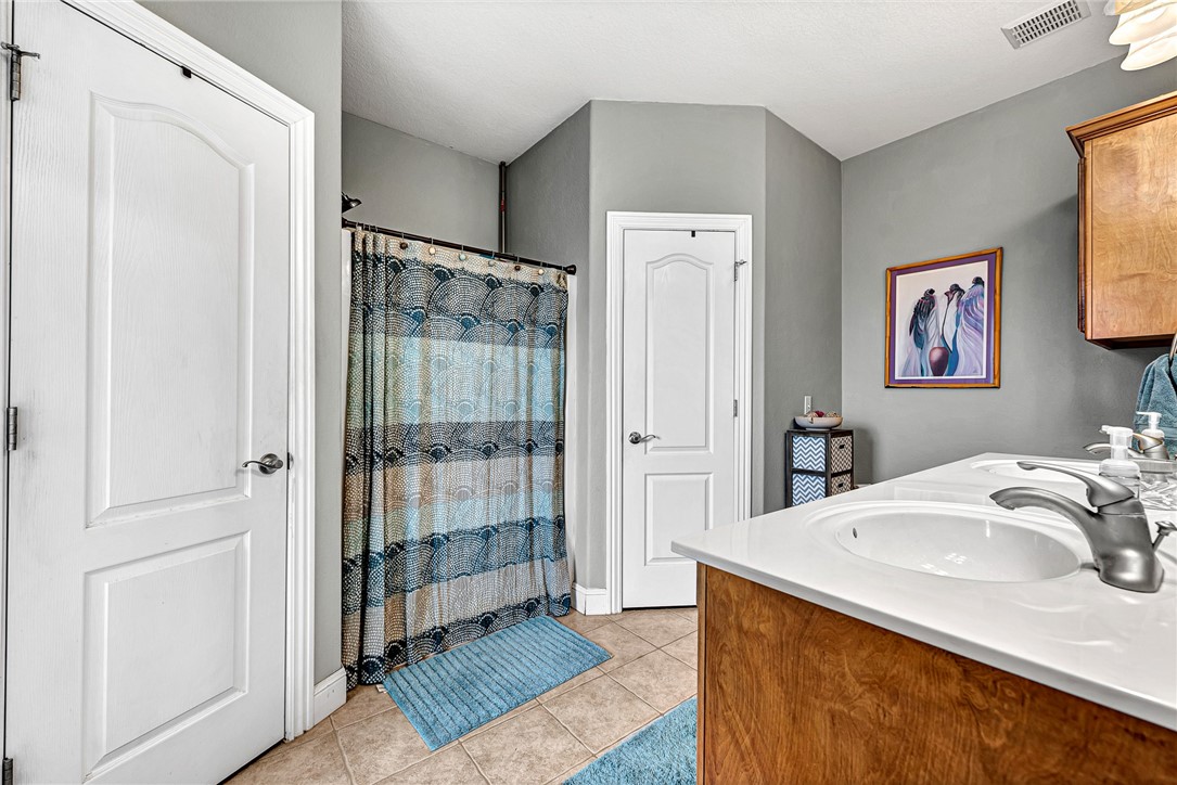 Bathroom with a double-sink vanity, wood cabinets, and a patterned blue shower curtain.