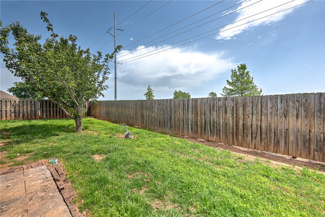 Fenced backyard with a grassy lawn, leafy tree, and small paved patio.