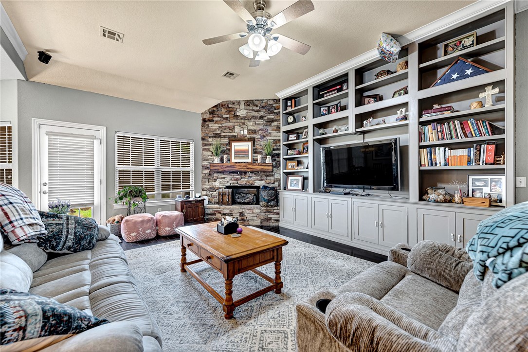 Furnished living room with a stone fireplace and built-in bookshelves surrounding a television.