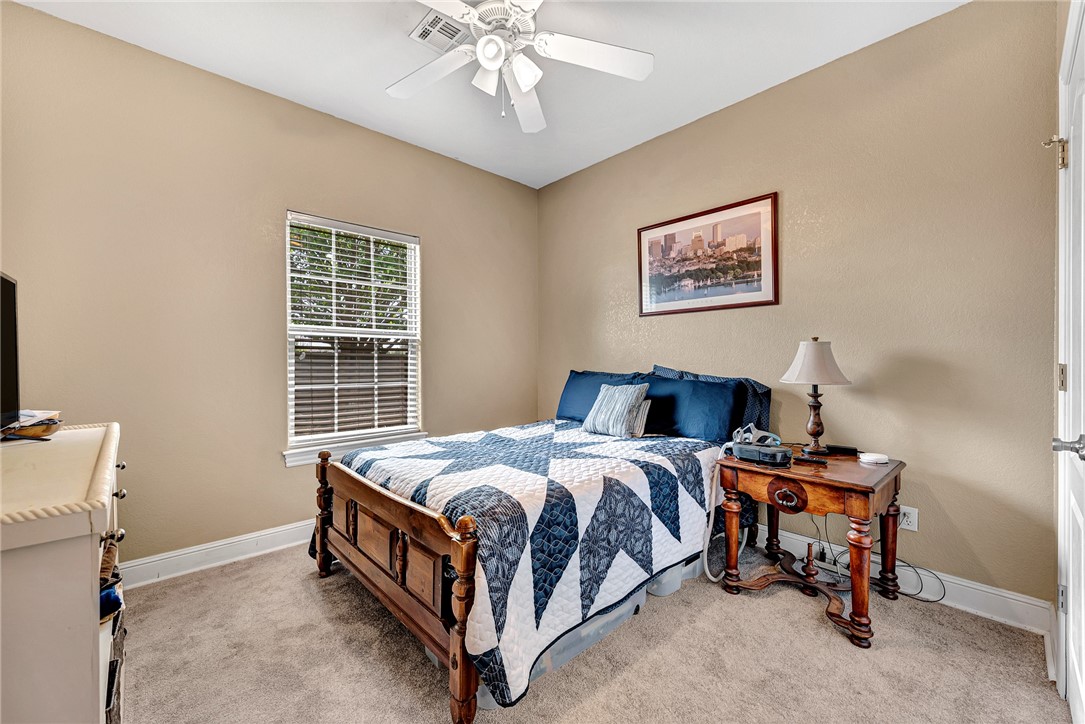 Bedroom with a wooden bed, blue-and-white quilt, window with blinds, and ceiling fan.