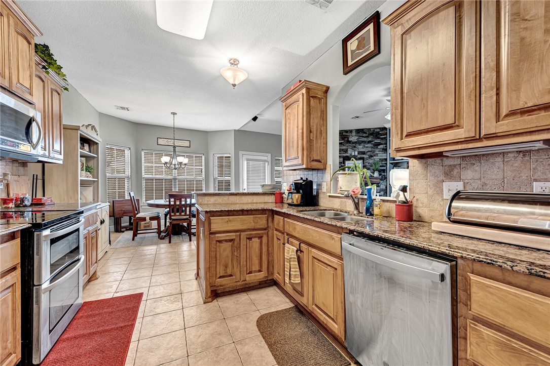 Kitchen with wood cabinetry, granite counters, a central island, and a dining area by the windows.