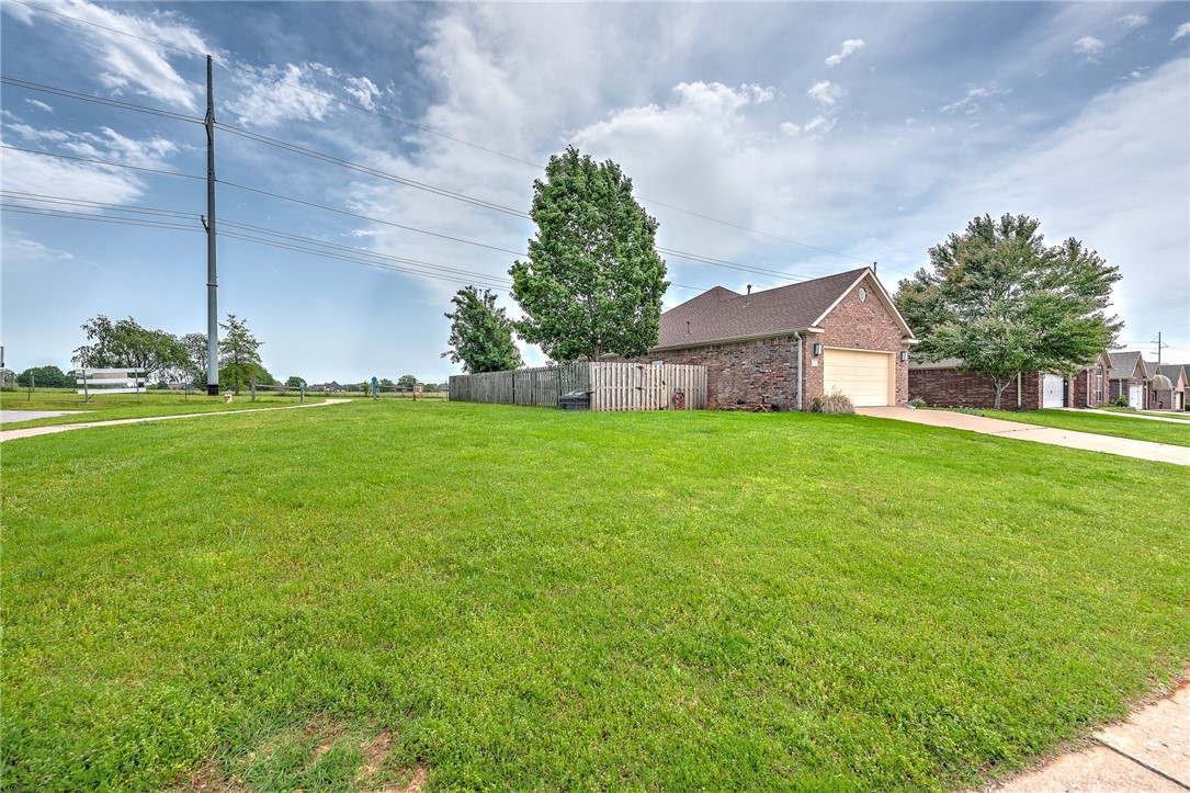 Brick home with an attached garage beyond a broad lawn and wooden side-yard fence.