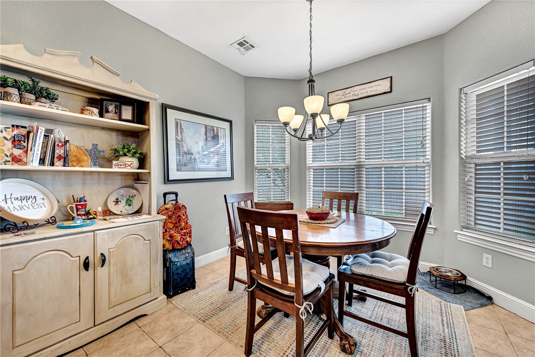 Dining room with a round wooden table, cream display hutch, and chandelier beside large windows.