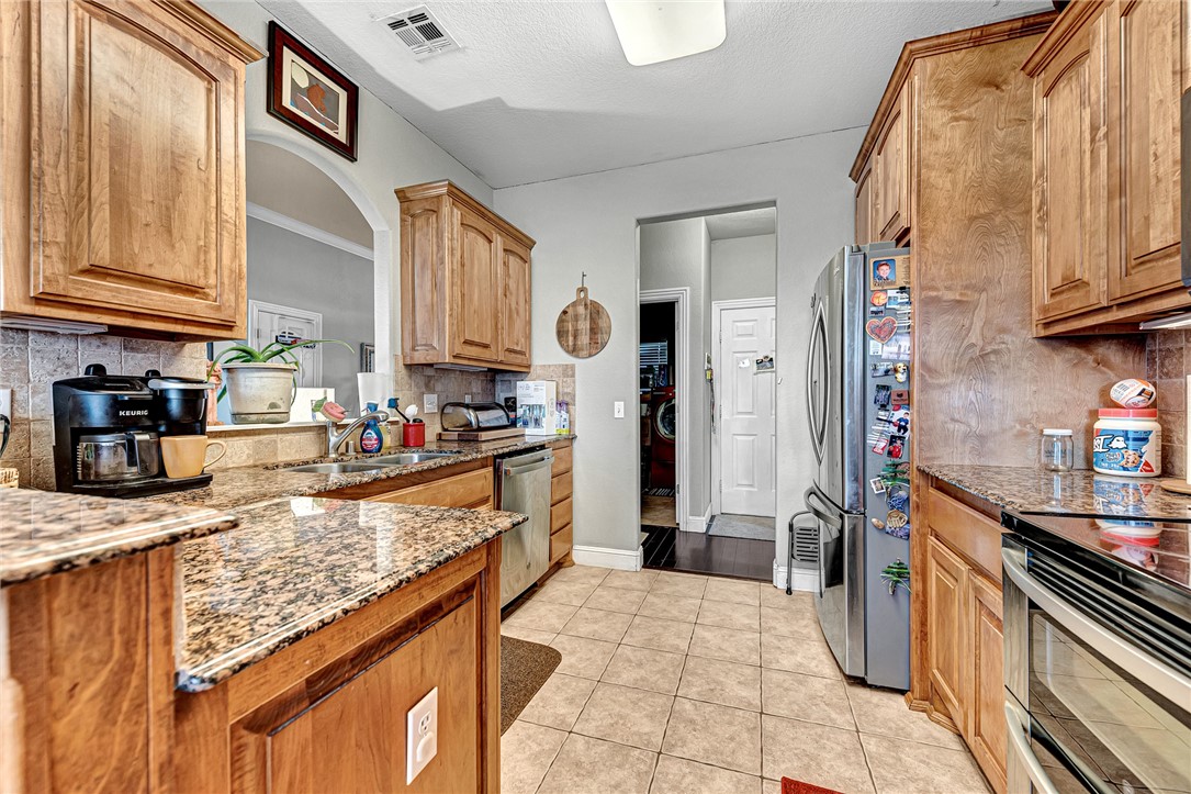 Kitchen with warm wood cabinets, granite counters, tiled floors, and stainless-steel appliances.