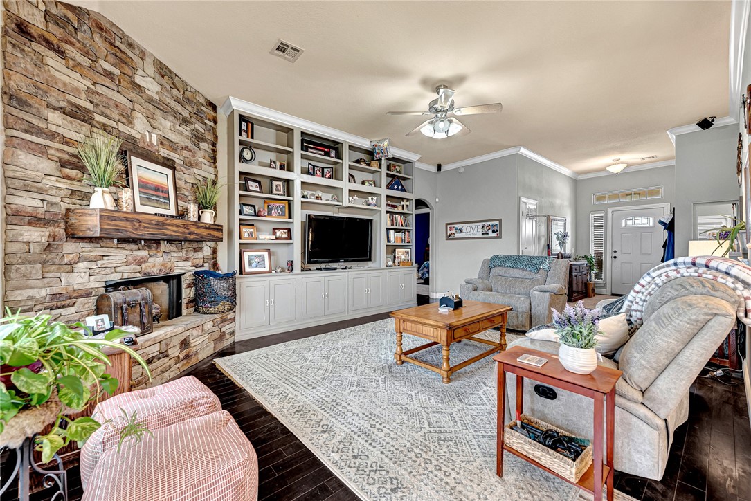 Living room with a stone fireplace, built-in TV shelving, gray seating, and a large patterned rug.