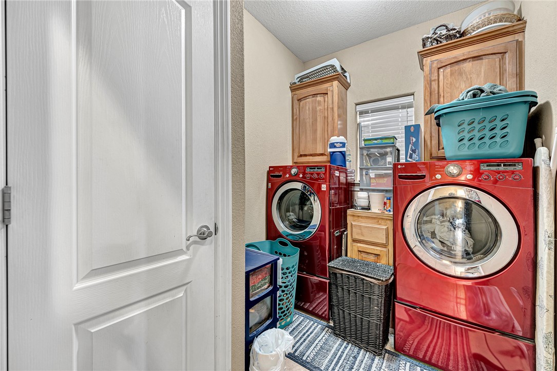 Laundry room with red front-loading washer and dryer beneath wood cabinets.