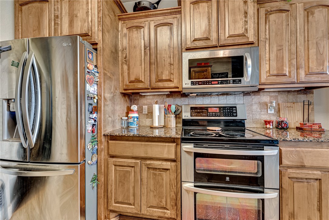 Kitchen with honey-toned wood cabinets, granite counters, and stainless steel appliances.